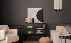 Nowoczesny salon z ciemnoszarą ścianą, kremową sofą i fotelem. Inspiracja, jak pomalować salon nowocześnie, z wykorzystaniem sztuki i tekstur.