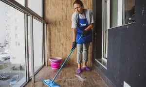 Kobieta w fartuchu myje podłogę z płytek na balkonie. Płyn do mycia podłóg z płytek tworzy pianę.