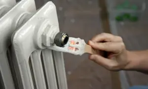 Oto jak pomalować kaloryfer: ręka z pędzlem pokrywa farbą metalową rurkę przy grzejniku.