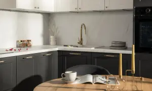 Elegancka kuchnia z ciemnymi szafkami i złotymi uchwytami. Na blacie słoiki z orzechami, wazonik i złota bateria. Na pierwszym planie stół z filiżanką i świecami.