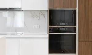 Nowoczesna kuchnia z dwoma wbudowanymi piekarnikami, jeden nad drugim. Ich wysokość idealnie komponuje się z drewnianą zabudową.