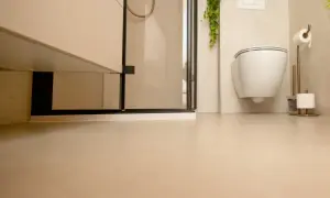 Nowoczesna łazienka z podwieszanym WC i prysznicem. Jasne ściany i podłoga tworzą spójną całość, a płytki na płytki dodają elegancji.