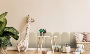 Uroczy pokój dziecięcy z pluszową żyrafą i zabawkami. W tle subtelne, łukowate klejenie paneli tapicerowanych tworzy przytulną atmosferę.