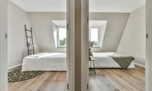 Jak podzielić pokój na dwa bez ściany? Dwa łóżka w jasnej sypialni z oknami dachowymi, oddzielone drzwiami.