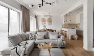 Przytulny salon w kolorach ziemi, z wygodną sofą, drewnianym stolikiem i otwartą kuchnią.