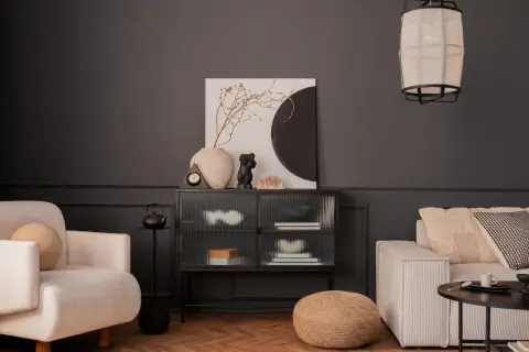 Nowoczesny salon z ciemnoszarą ścianą, kremową sofą i fotelem. Inspiracja, jak pomalować salon nowocześnie, z wykorzystaniem sztuki i tekstur.