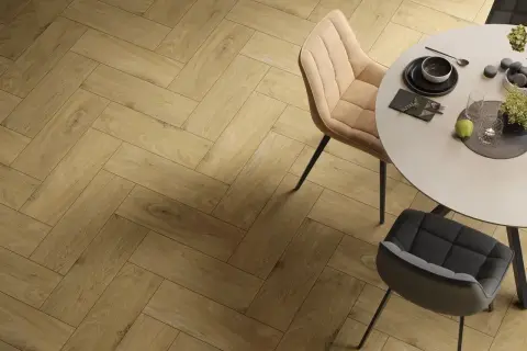 Eleganckie wzory układania płytek drewnopodobnych w jodełkę tworzą ciepłą atmosferę wokół okrągłego stołu z krzesłami.