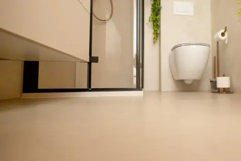 Nowoczesna łazienka z podwieszanym WC i prysznicem. Jasne ściany i podłoga tworzą spójną całość, a płytki na płytki dodają elegancji.