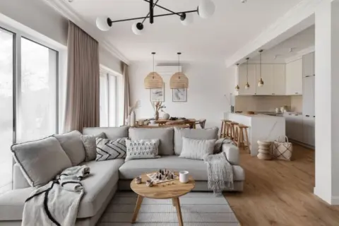 Przytulny salon w kolorach ziemi, z wygodną sofą, drewnianym stolikiem i otwartą kuchnią.
