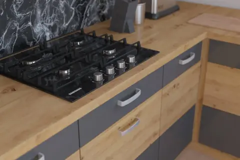Nowoczesna kuchnia z czarną płytą gazową na blacie dąb artisan. Szare fronty szafek z metalowymi uchwytami.