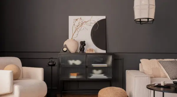 Nowoczesny salon z ciemnoszarą ścianą, kremową sofą i fotelem. Inspiracja, jak pomalować salon nowocześnie, z wykorzystaniem sztuki i tekstur.