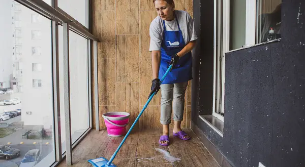 Kobieta w fartuchu myje podłogę z płytek na balkonie. Płyn do mycia podłóg z płytek tworzy pianę.
