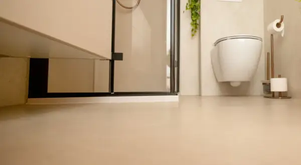 Nowoczesna łazienka z podwieszanym WC i prysznicem. Jasne ściany i podłoga tworzą spójną całość, a płytki na płytki dodają elegancji.