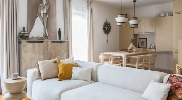 Jasny salon z sofą, stołem i krzesłami w stylu organic modern. Drewniane meble, naturalne tkaniny i subtelne dekoracje tworzą przytulną atmosferę.