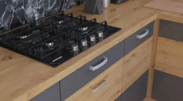 Nowoczesna kuchnia z czarną płytą gazową na blacie dąb artisan. Szare fronty szafek z metalowymi uchwytami.
