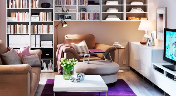 Małe mieszkanie inspiracje: przytulny salon z regałami pełnymi książek, wygodnym fotelem i stolikiem kawowym.