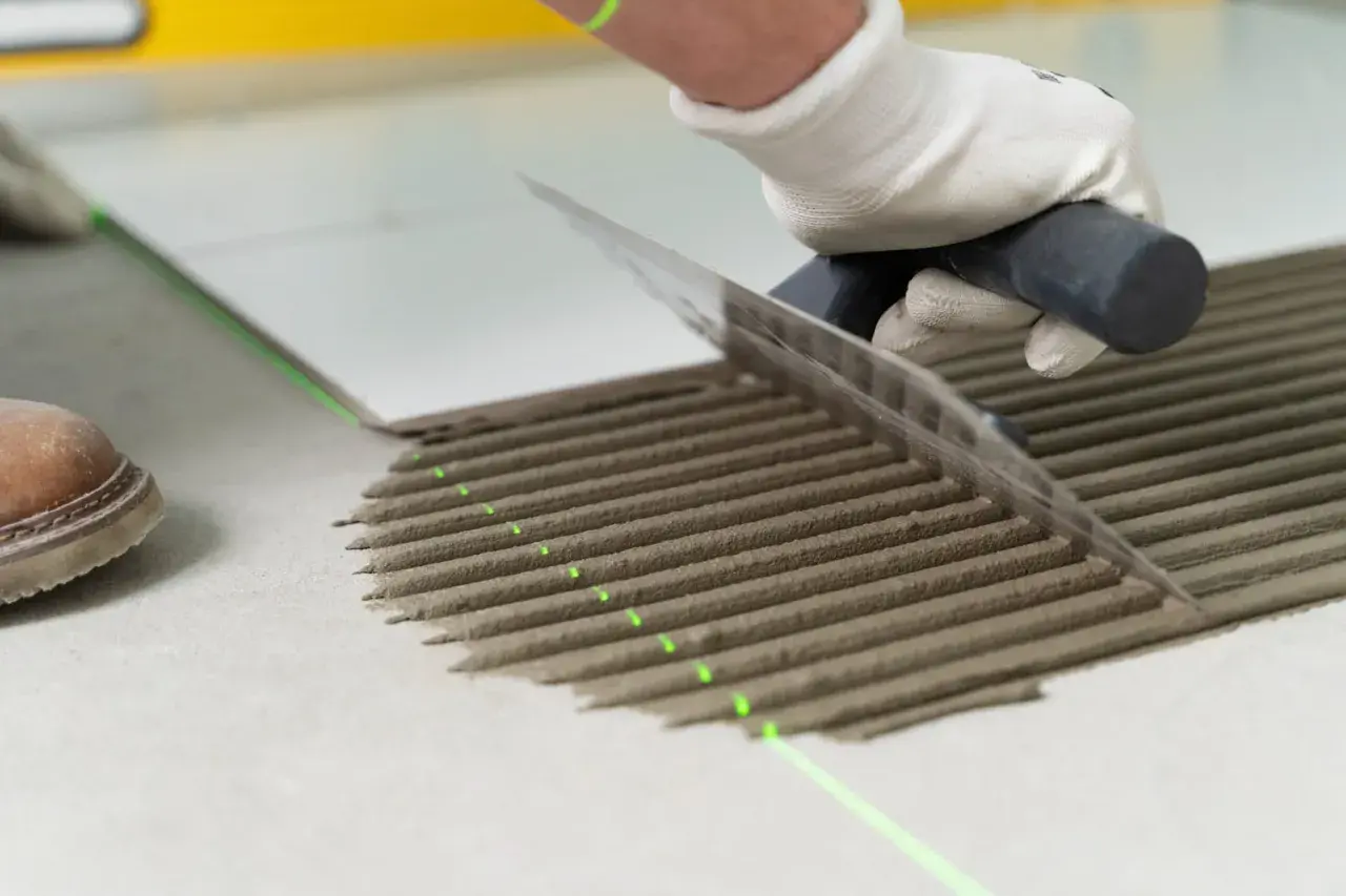 Równomierne rozprowadzanie kleju pod płytki za pomocą kielni. Precyzyjne linie kleju i zielona linia lasera zapewniają idealne ułożenie.