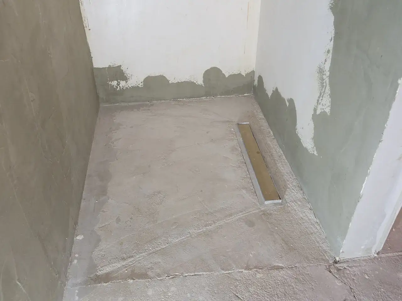 Niedawno położony beton na podłodze prysznicowej, z widocznym odpływem liniowym. Trwają prace wykończeniowe, zastanawiamy się, czy akryl jest wodoszczelny.
