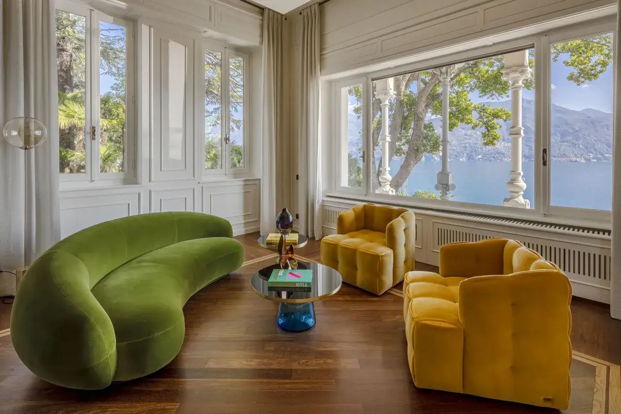 Salon w stylu art deco z zieloną sofą i żółtymi fotelami, z widokiem na jezioro i góry.