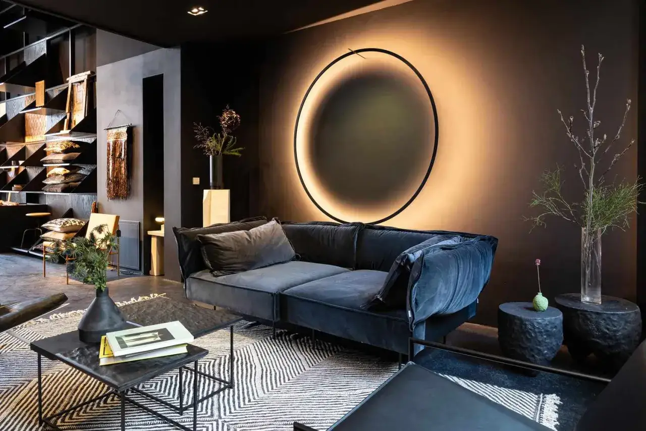 Nowoczesny salon z granatową kanapą i okrągłym oświetleniem akcentowym na ścianie.