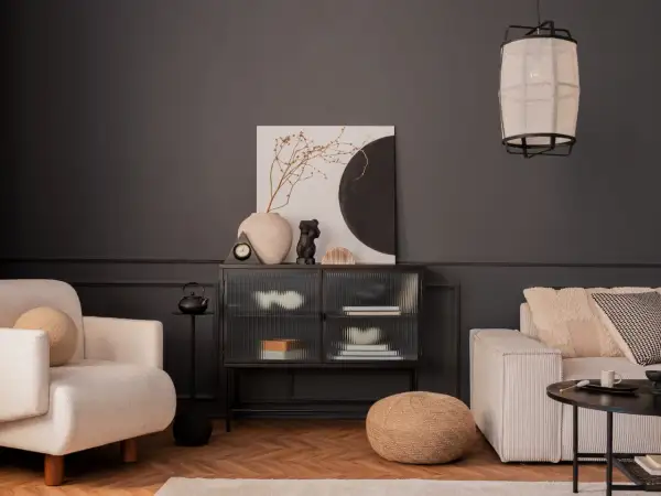 Nowoczesny salon z ciemnoszarą ścianą, kremową sofą i fotelem. Inspiracja, jak pomalować salon nowocześnie, z wykorzystaniem sztuki i tekstur.