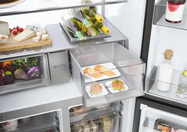 Wnętrze lodówki: świeże warzywa, sery, łosoś, tatary, butelki wina i napojów.