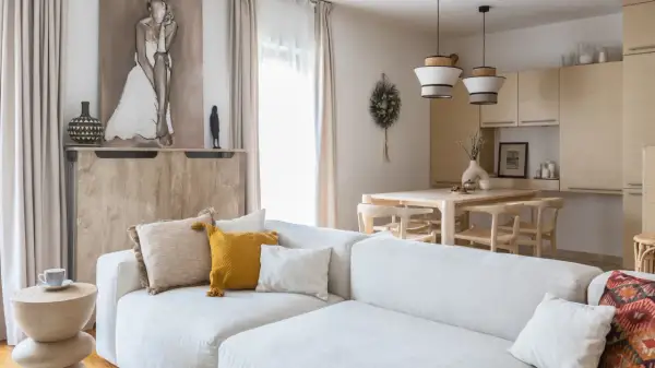 Jasny salon z sofą, stołem i krzesłami w stylu organic modern. Drewniane meble, naturalne tkaniny i subtelne dekoracje tworzą przytulną atmosferę.