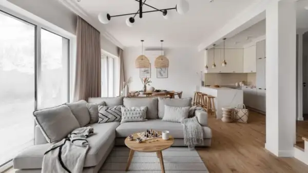 Przytulny salon w kolorach ziemi, z wygodną sofą, drewnianym stolikiem i otwartą kuchnią.